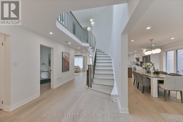 Open concept foyer with a curved staircase, light wood floors, and view of dining area and kitchen. - 49 Cygnus Drive, Richmond Hill