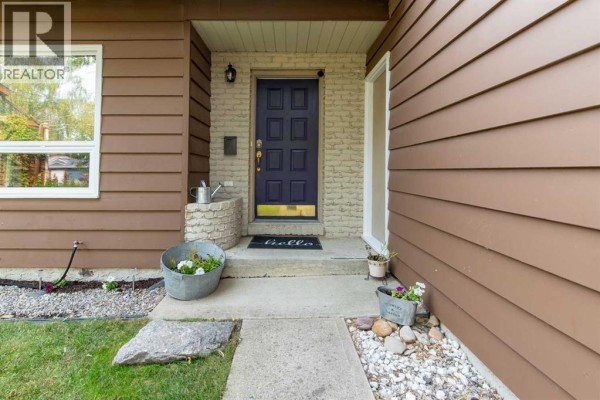 Close-up of the front entrance with a dark blue door, brick and stucco detailing, and potted plants. - 49 Iroquois Crescent W, Lethbridge