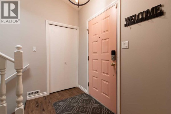 Entrance hallway with a pale pink front door, closet, staircase railing, and a welcome sign. - 49 Iroquois Crescent W, Lethbridge