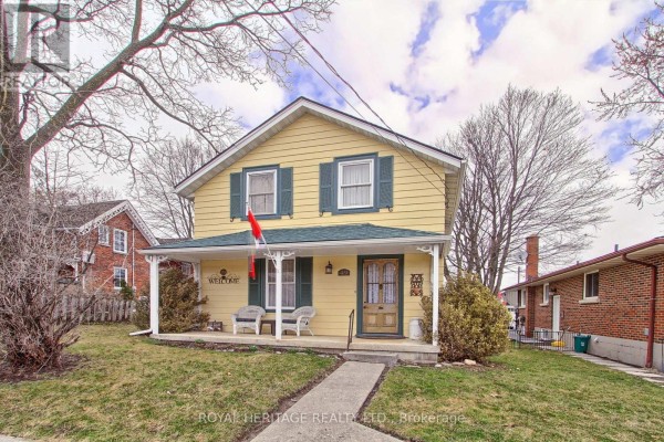 Side view of a yellow house with a covered porch and a Canadian flag visible. - 49 John Street E, Bradford West Gwillimbury