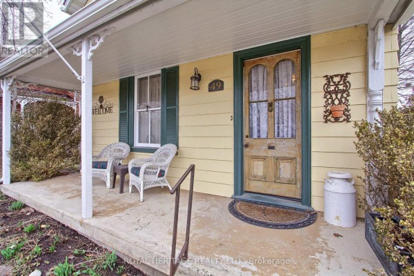 Close-up of the front porch showing wicker chairs, a wooden door, and a milk can. - 49 John Street E, Bradford West Gwillimbury