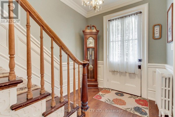 Interior hallway with a wooden staircase, grandfather clock, and white door with curtains. - 49 John Street E, Bradford West Gwillimbury