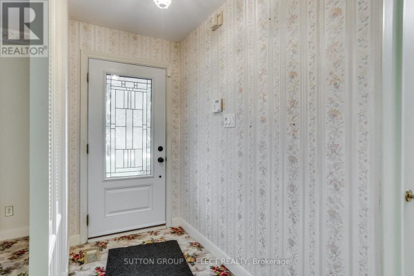 Interior entryway with white door, patterned wallpaper, and floral carpet. - 49 Mcleod Crescent, London North