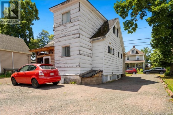 Side and back view of the house showing a gravel driveway with cars parked. - 49 Mcsweeney Avenue, Moncton