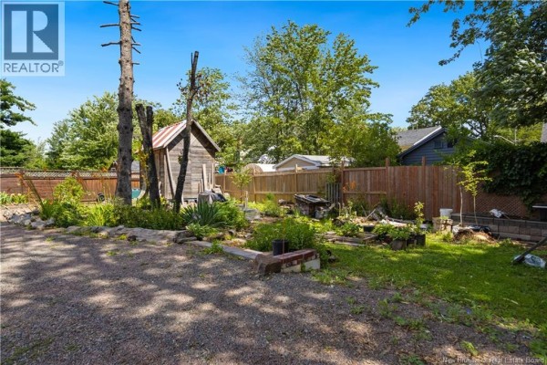Backyard view with raised garden beds, a wooden fence, and mature trees. - 49 Mcsweeney Avenue, Moncton