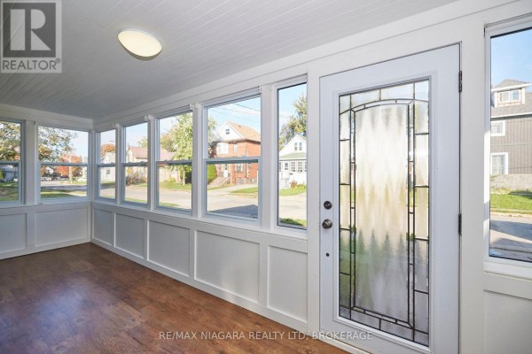 Interior sunroom with white walls, wood floor, and large windows overlooking the street. - 49 Randolph Street, Welland