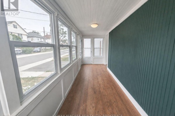 Interior sunroom with green beadboard walls, wood floor, and large windows. - 49 Randolph Street, Welland