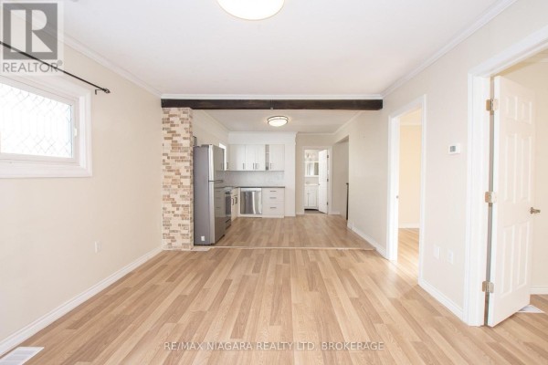 Living area with wood floors, beige walls, and an opening to a kitchen. - 49 Randolph Street, Welland