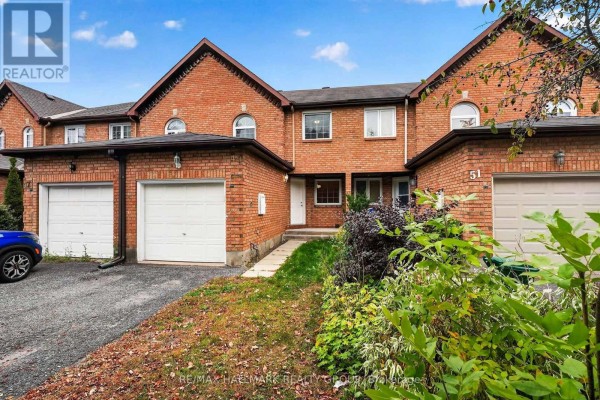Exterior front view of red brick townhouses with white garage doors. - 49 Robarts Crescent, Ottawa