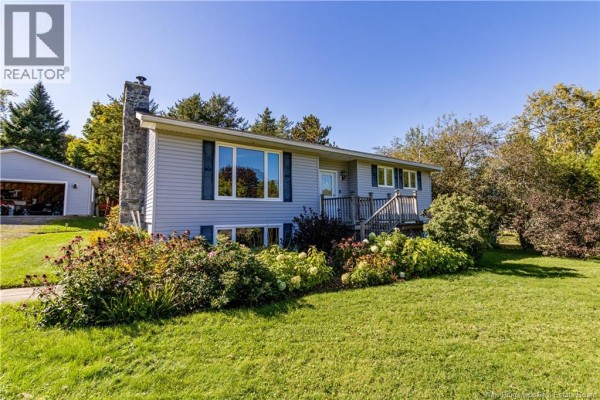 Side exterior view of the light grey house with a stone chimney and flower beds. - 49 Yeomans Road, Mill Brook