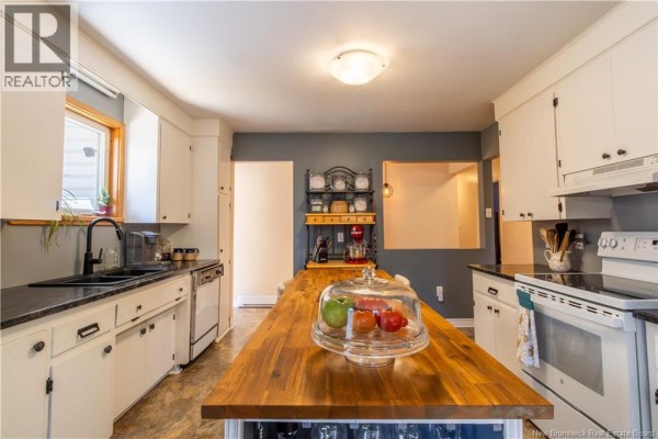 Kitchen with white cabinets, black countertops, a wooden island, and stainless steel appliances. - 49 Yeomans Road, Mill Brook