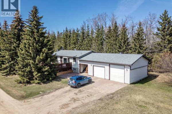 Front exterior of the house with a deck, attached double garage, and surrounding evergreen trees. - 49059 Rge Rd 265, Rural Leduc County