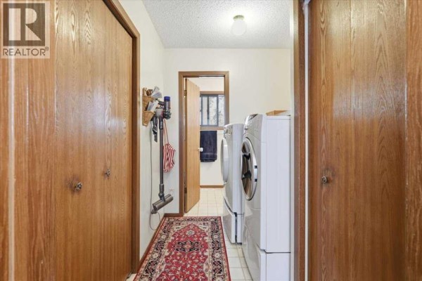 Laundry room with white washer and dryer, wood-paneled closets, and a red patterned rug. - 49059 Rge Rd 265, Rural Leduc County
