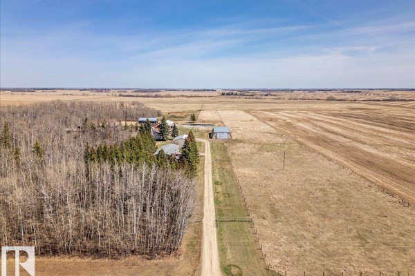 Aerial perspective looking down a long gravel driveway towards the farm buildings and wooded areas. - 49059 Rge Road 265, Rural Leduc County