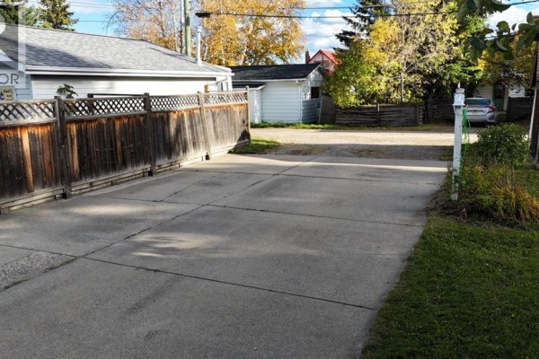 Concrete driveway leading towards a wooden fence with a street and other buildings in the background. - 4907 7 Avenue, Edson
