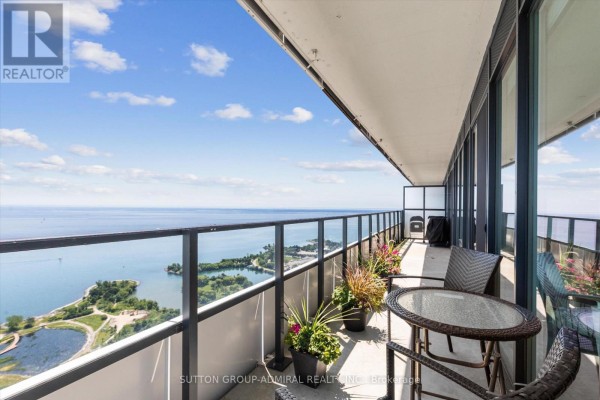 Spacious balcony with glass railings, a table, chairs, and potted plants overlooking a large body of water. - 4908 - 30 Shore Breeze Drive, Toronto