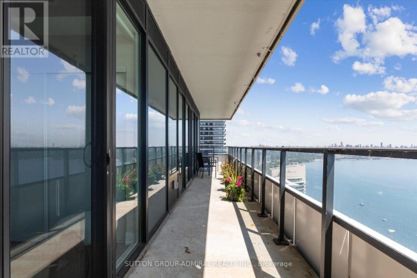 Long balcony with glass railings, outdoor furniture, and views of the city skyline and lake. - 4908 - 30 Shore Breeze Drive, Toronto