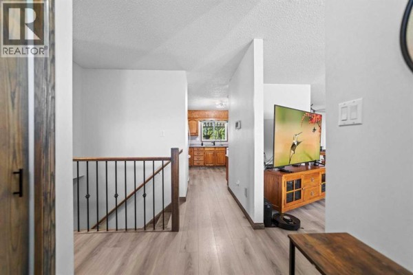 Interior hallway with light wood-look flooring and a staircase with black railing, leading to a kitchen. - 4908 56 Street W, Forestburg