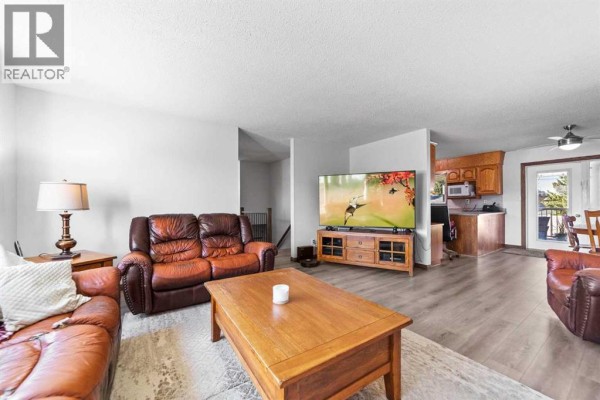 Living room with a large television, leather sofas, coffee table, and view into the kitchen and dining area. - 4908 56 Street W, Forestburg