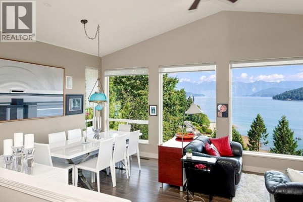 Living room with black leather sofas, large windows, and access to an outdoor deck. - 491 Woodland Avenue, Gibsons
