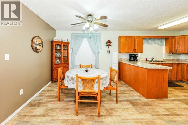 Dining area with a round table and chairs, next to a large window and hutch. - 4912 56 Avenue, Ryley