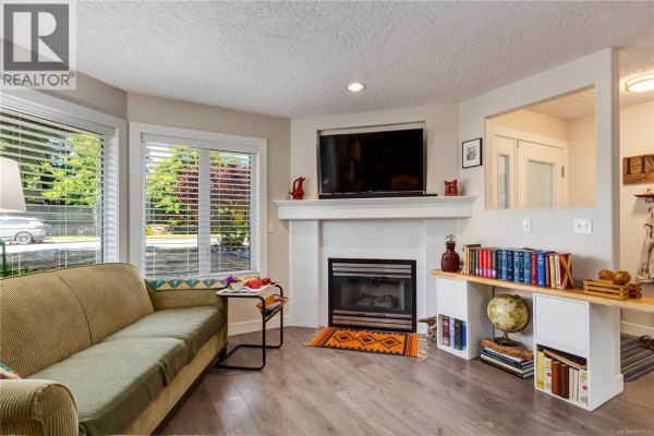 Living room with a rocking chair, fireplace, shelving with books, and view into dining area. - 4915 Denford Pl, Nanaimo