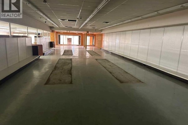 Another angle of the empty interior with visible flooring and natural light from windows. - 4919 50 Street, Rocky Mountain House