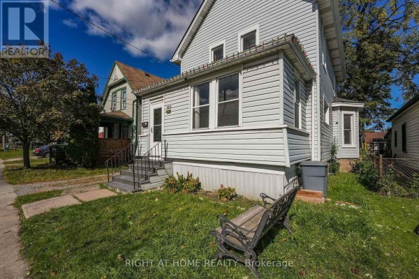 A living room with hardwood floors, plants, a dog crate, and a dresser. - 4919 Huron Street, Niagara Falls