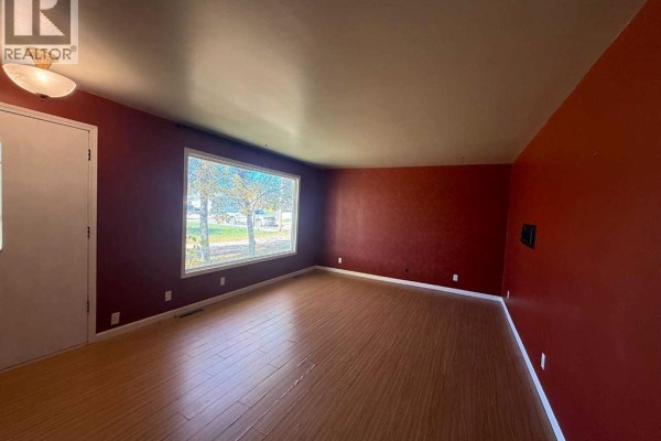 Living room with red walls, a large picture window, and light wood laminate flooring. - 4925 52 Avenue, Eaglesham