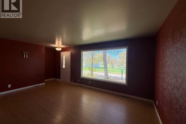 Living room with red textured walls, a large window, and light wood floors. - 4925 52 Avenue, Eaglesham