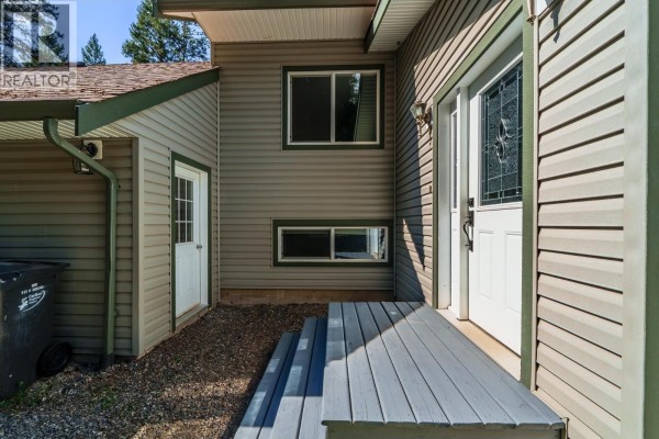 Front entrance of a grey sided house with a white door, a small porch, and a side door. - 4931 Kyllo Road, 108 Mile Ranch