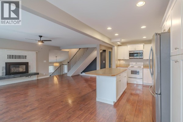 An open concept living room with a fireplace and a kitchen with white cabinets and stainless steel appliances. - 4931 Kyllo Road, 108 Mile Ranch