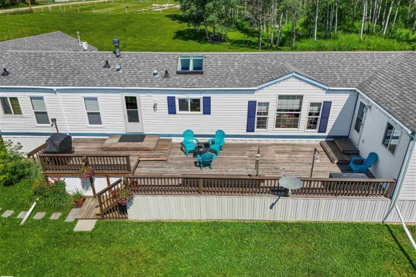 Close-up aerial view of a wooden deck on a white mobile home with blue chairs and outdoor furniture. - 49327 Rge Rd 53, Rural Brazeau County