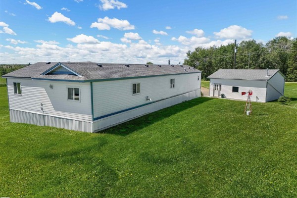 Side exterior view of a white mobile home and a small white outbuilding with a red windmill in a field. - 49327 Rge Rd 53, Rural Brazeau County