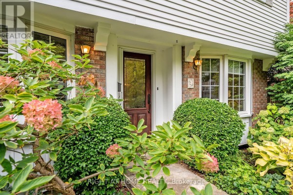 Close-up of the front entrance with a wooden door, brick accents, and blooming pink hydrangeas. - 494 Dorland Road, Oakville