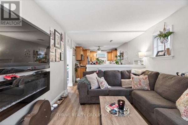 Living room with a large sectional sofa, wall-mounted TV, and open kitchen view. - 494 Highbury Avenue N, London East