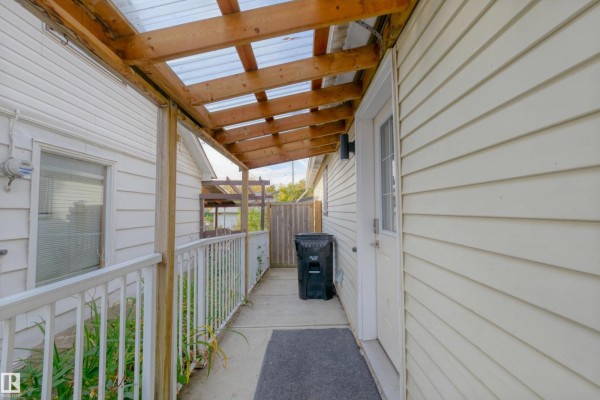 Covered walkway with a clear roof leading to a door on a light yellow house, next to a trash bin. - 4947 49 Avenue, Barrhead