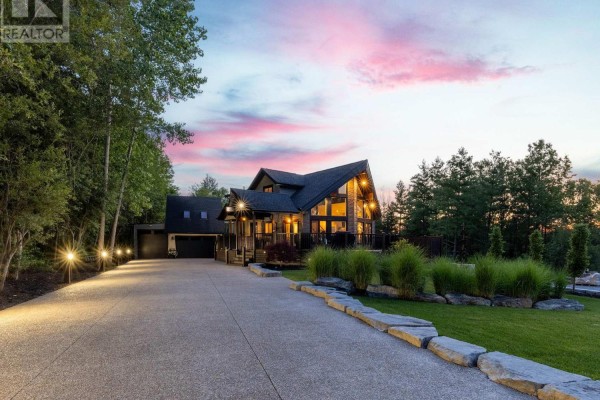 Aerial view of a modern house with dark wood siding, extensive decking, and surrounding green trees. - 4949 Lyon's Parkway, Niagara Falls
