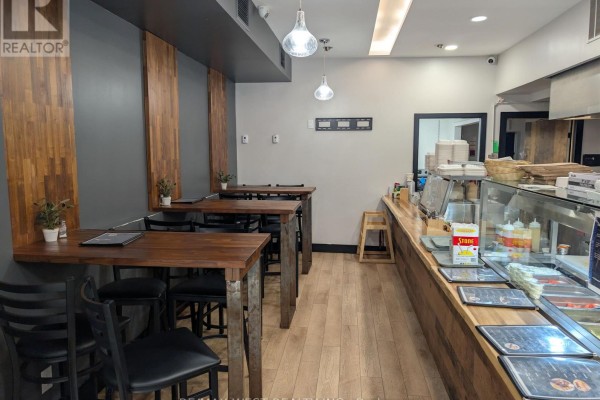 Dining area with wooden tables and chairs against a dark grey wall with wood accents. - 495 Bloor Street W, Toronto