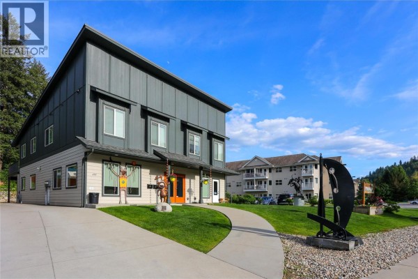 Corner view of a modern commercial building with a sidewalk, sculpture, and apartment buildings in the background. - 495 Columbia Street, Castlegar