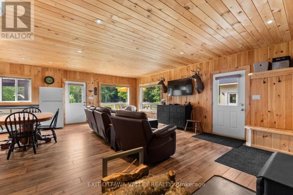 Living room with wood-paneled walls and ceiling, leather recliners, dining table, and kitchen. - 495 Gravel Pit Lane, Wollaston