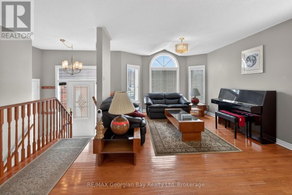 Living room with hardwood floors, black leather sofas, a coffee table, and a piano. - 495 Shewfelt Crescent, Midland