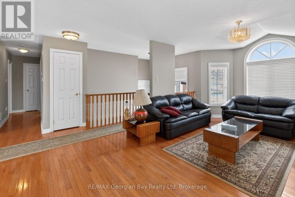 Spacious living room with hardwood floors, black sofas, a coffee table, and adjacent hallway. - 495 Shewfelt Crescent, Midland