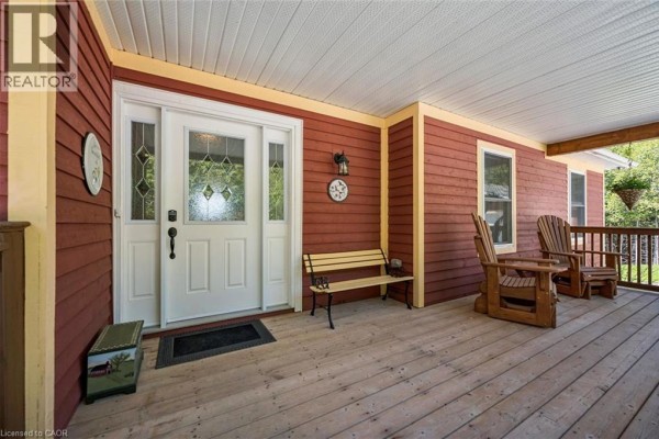 Covered front porch with red siding, white double doors, bench, and two Adirondack chairs. - 495190 Traverston Road, Markdale