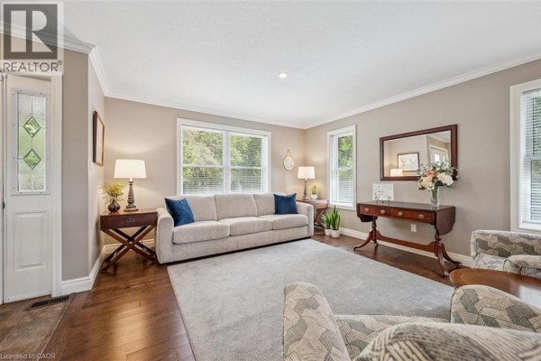 Living room with beige walls, grey rug, light grey sofa, dark wood floors, and two armchairs. - 495190 Traverston Road, Markdale