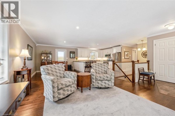 Open-concept living and kitchen area with patterned armchairs, wood floors, and white kitchen cabinets. - 495190 Traverston Road, Markdale