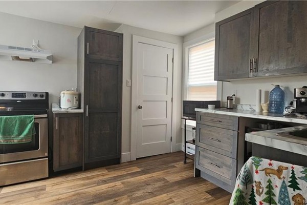 Kitchen with dark wood cabinets, stainless steel stove, white countertop, and wood-look vinyl flooring. - 496 Robinson Street, Moncton