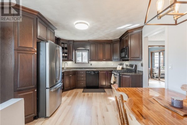 Kitchen with dark wood cabinets, stainless steel appliances, a dishwasher, and a wooden dining table. - 4961 Coleen Avenue, Hanmer