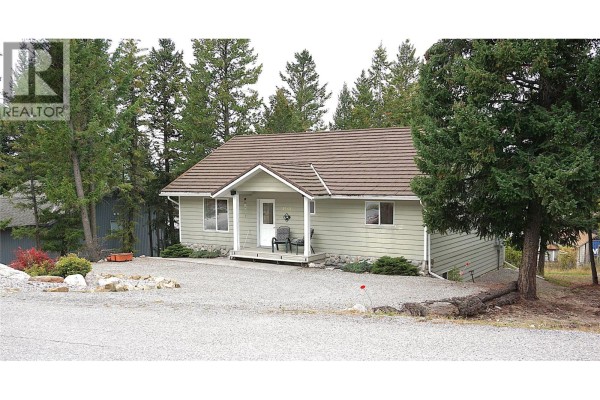 Side view of a light green, single-story house with a brown roof and pine trees. - 4969 Mountain Side Road, Fairmont Hot Springs