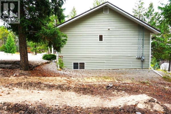 Back side of a light green house showing vinyl siding, two small windows, and a ventilation grate. - 4969 Mountain Side Road, Fairmont Hot Springs